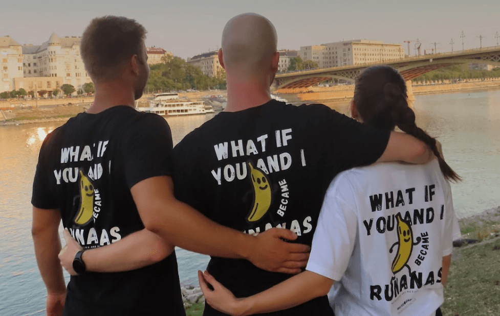 Three friends in Runanas shirts standing together by the Danube at sunset